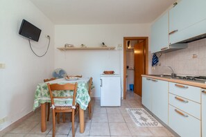A compact kitchen with a dining table, chairs, a small refrigerator, and a TV mounted on the wall. - APPARTAMENTI I LIMONI - APPARTAMENTI I LIMONI - BILO 4 (Campo nell'Elba)