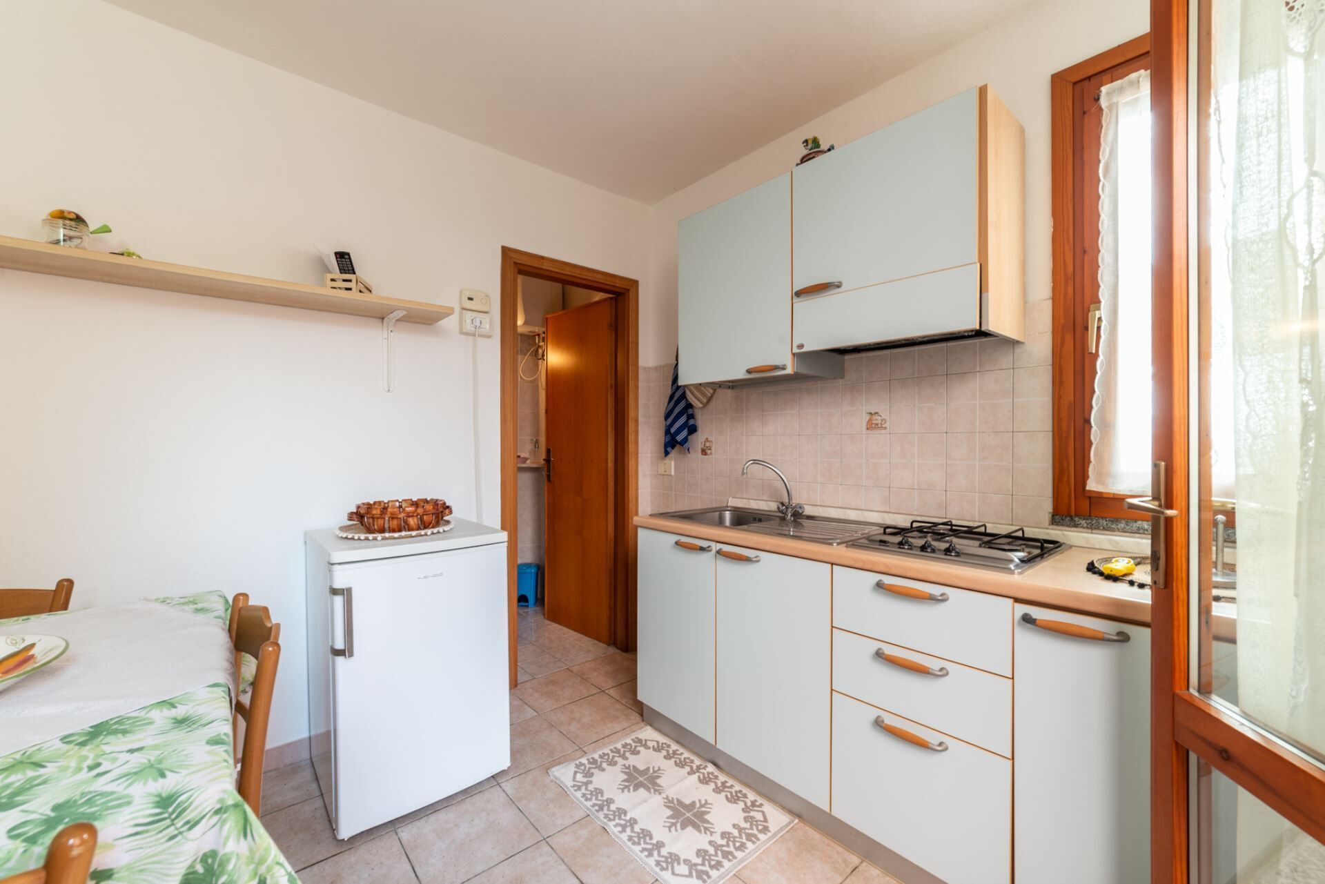 Een kleine keuken met een koelkast, fornuis, gootsteen en houten kastjes.
