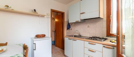 Een kleine keuken met een koelkast, fornuis, gootsteen en houten kastjes.