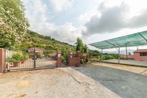 A gated entrance to a property with a gravel driveway, a covered area with a green roof, and a hillside with vegetation. - APPARTAMENTI I LIMONI - APPARTAMENTI I LIMONI - BILO 4 (Campo nell'Elba)