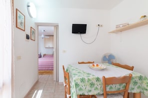 A room with a dining table, chairs, a television mounted on the wall, and a bed in the adjacent room. - APPARTAMENTI I LIMONI - APPARTAMENTI I LIMONI - BILO 4 (Campo nell'Elba)