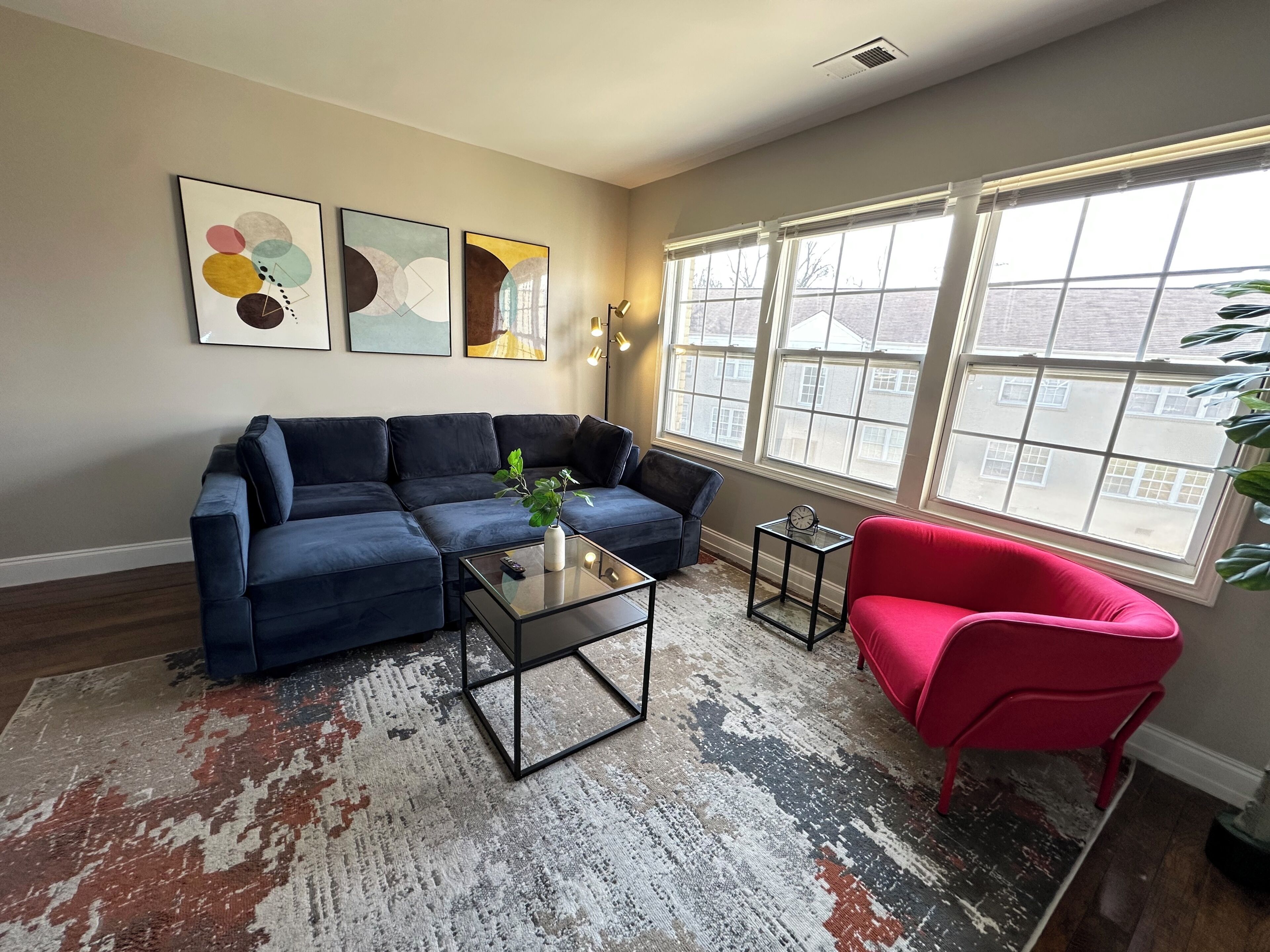 A living room with a sectional sofa, a red armchair, a coffee table, and a large window with a view of buildings.