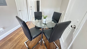 A modern dining area with a glass table surrounded by four black chairs, a small potted plant, and a white door in the background. - 1BR Business Suite with Parking Near Downtown Birmingham (Birmingham)