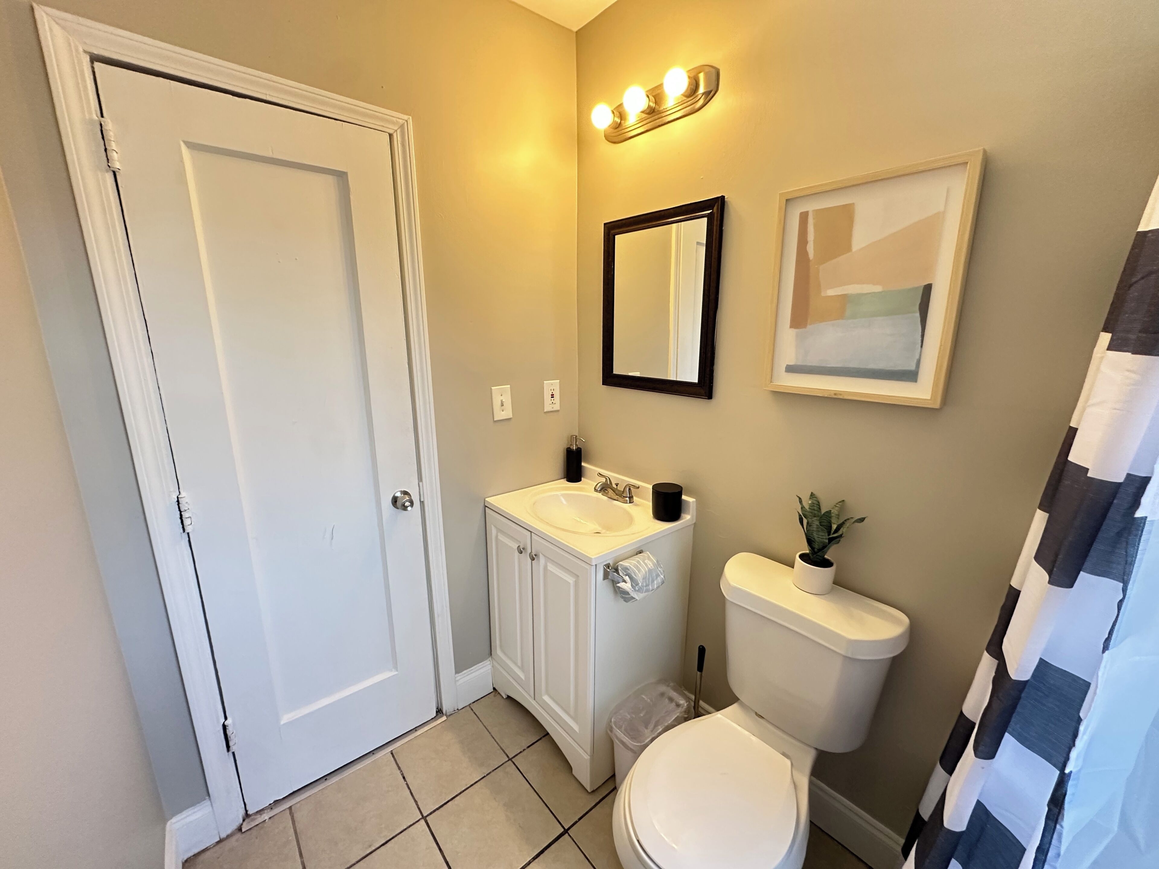 A bathroom with a toilet, sink, mirror, and a shower curtain.