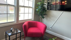A room with a red armchair, a glass table with a clock, a potted plant, and a wall-mounted TV displaying the Netflix logo. - 1BR Business Suite with Parking Near Downtown Birmingham (Birmingham)