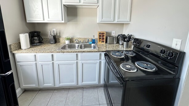 A kitchen with white cabinets, a black stove, and a granite countertop. - 1BR Business Suite with Parking Near Downtown Birmingham (Birmingham)