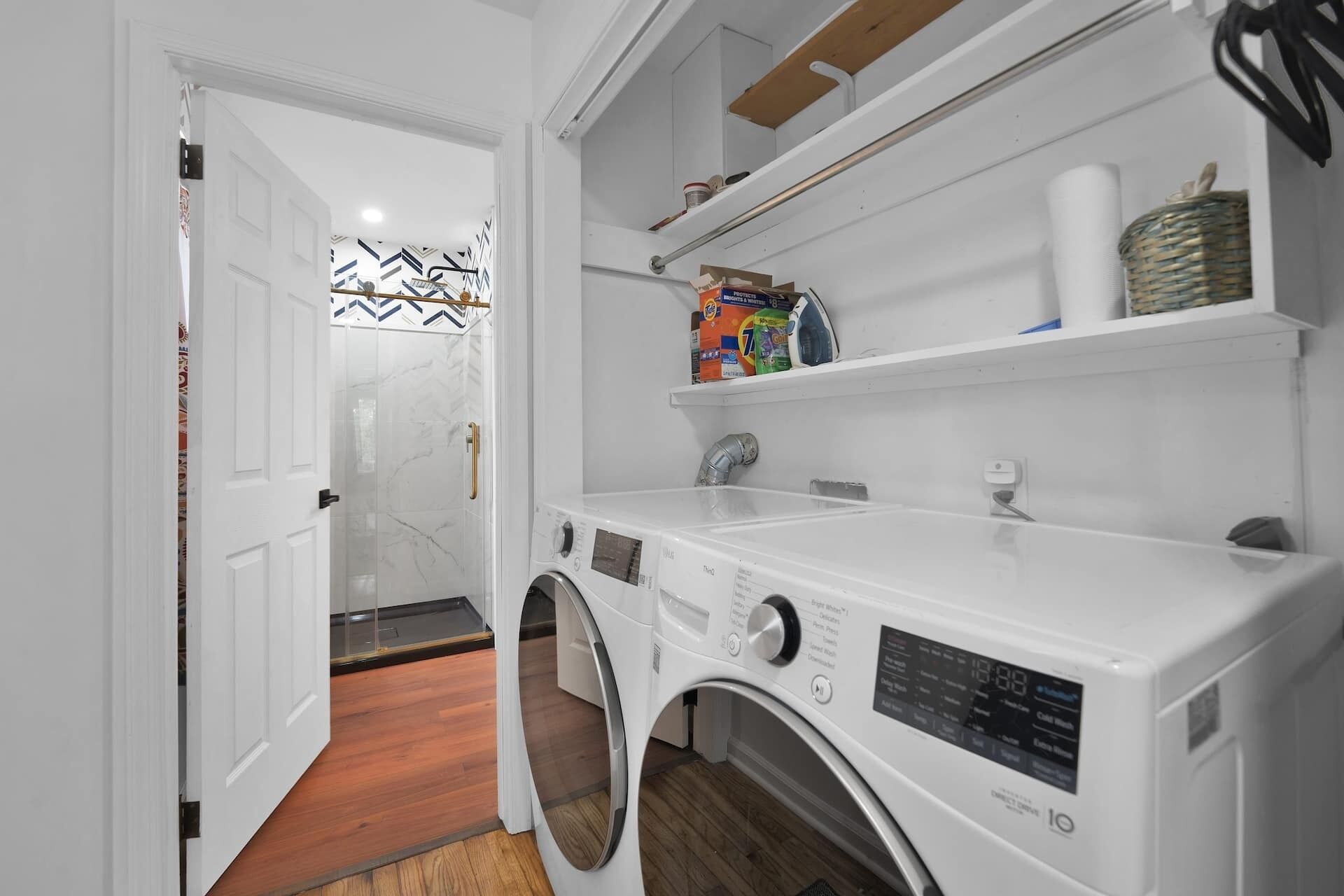 A laundry area with a front-loading washing machine, shelves with cleaning supplies, and a patterned wall.
