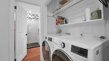 A laundry area with a front-loading washing machine, shelves with cleaning supplies, and a patterned wall.