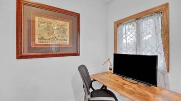 Una habitación con un escritorio de madera, una silla negra, un mapa enmarcado en la pared y una ventana con cortinas estampadas.