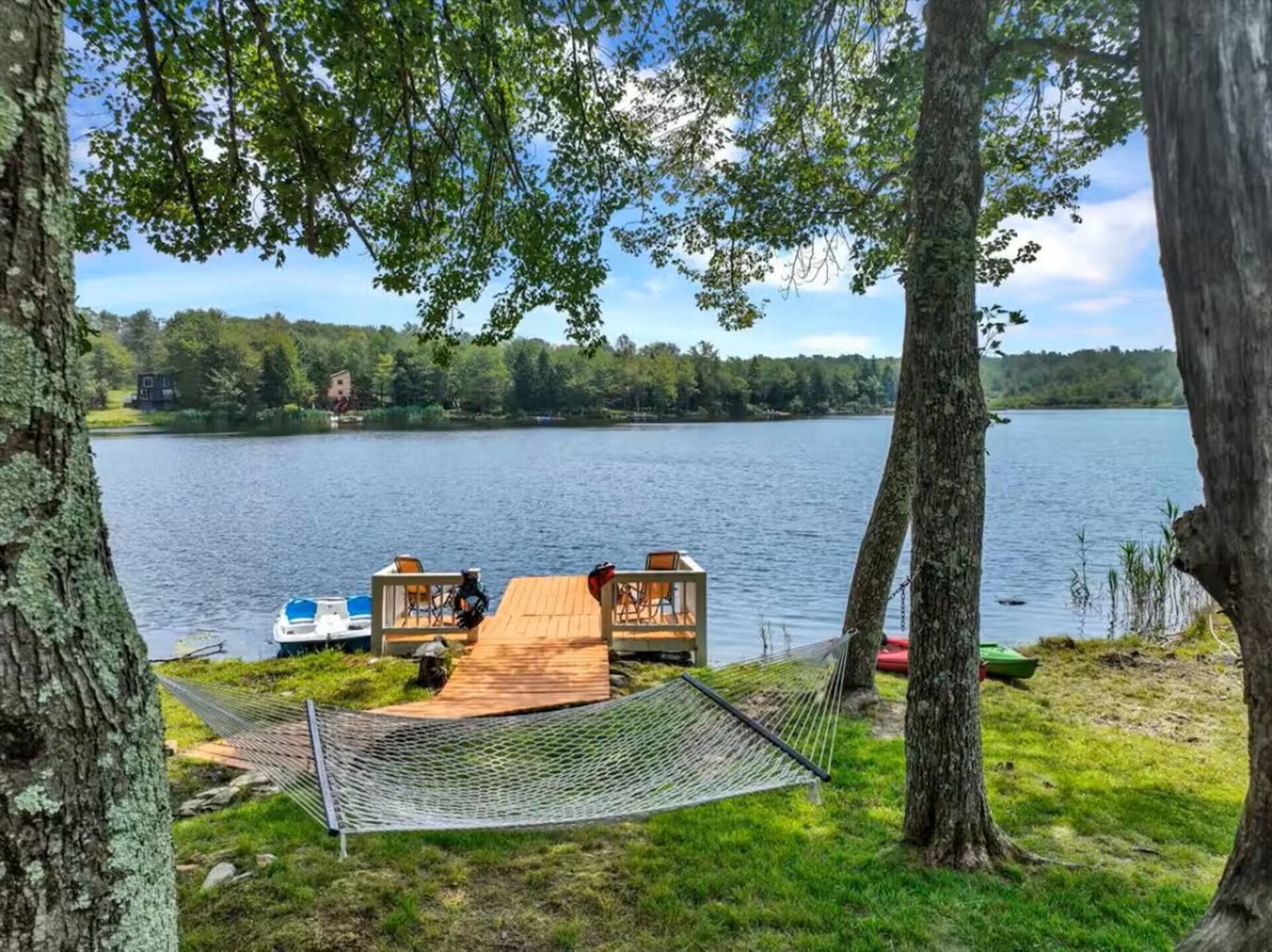 A lakeside view with a wooden dock, a hammock, and a small boat.