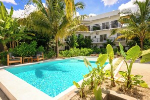 Une piscine entourée d’une végétation luxuriante et un immeuble à plusieurs étages doté de balcons.