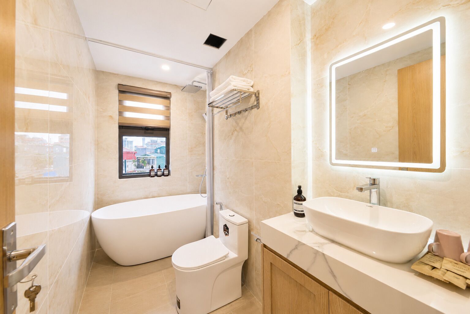 Un baño moderno con una bañera independiente, un inodoro, un tocador con un espejo grande y una ventana con vistas a edificios.