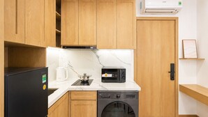 Cocina compacta con armarios de madera, microondas integrado, tetera y lavadora.
