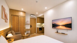 Habitación de hotel con cama, televisión, escritorio, silla, lámpara y vistas a un lago al atardecer.