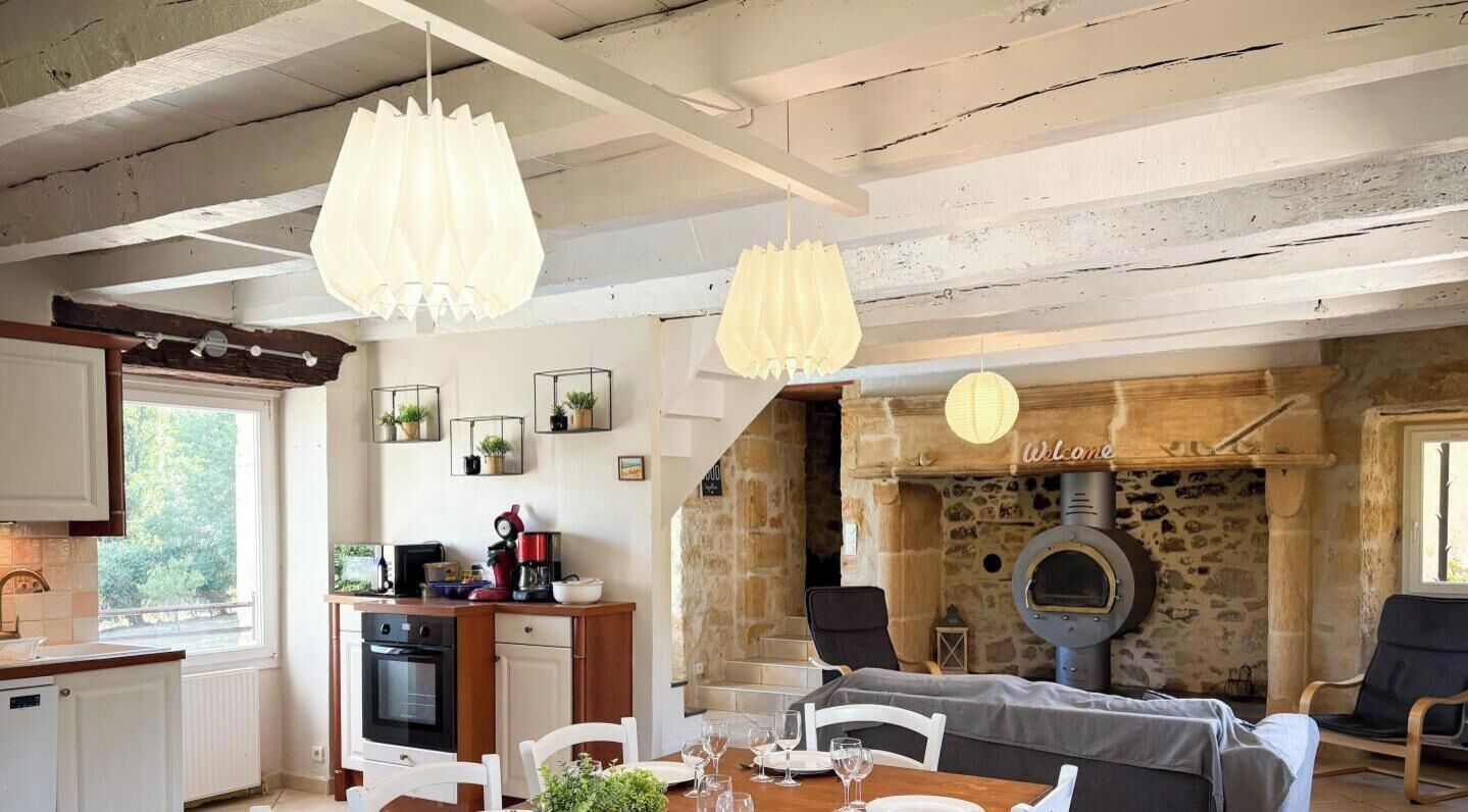 A rustic kitchen with a stone wall, a wood-burning oven, and a dining area with a table set for two.