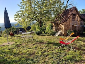A rustic stone house with a sloped roof, surrounded by a grassy yard with a tree and outdoor furniture. - Gîtes de France® - La Rosalie (ESTAL)