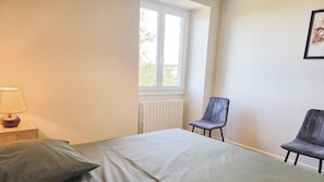 A bedroom with a bed, a window, a chair, and a lamp. - Gîtes de France® - La Rosalie (ESTAL)