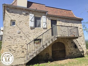 A stone building with a balcony, a staircase, and a door. - Gîtes de France® - La Rosalie (ESTAL)