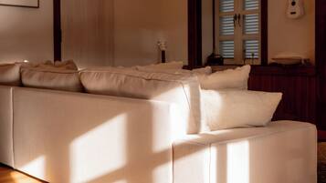 A large sectional sofa with a light-colored fabric, positioned in a room with wooden flooring and a sloped ceiling.