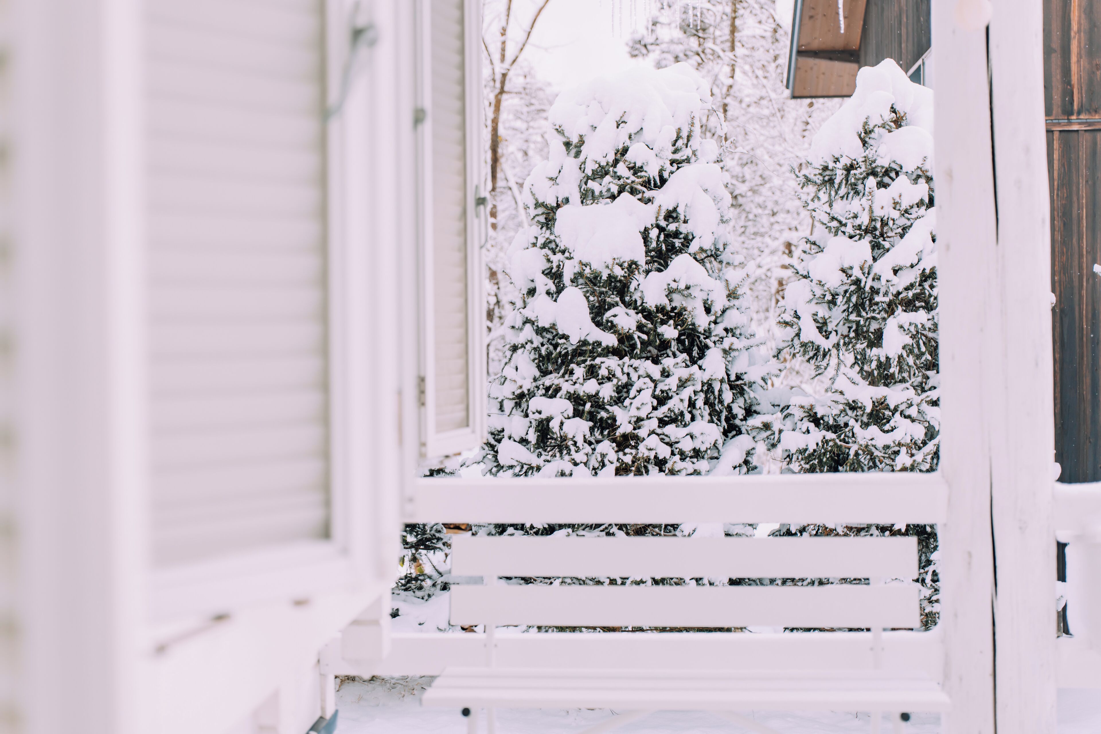 A snow-covered porch with a white railing and a bench.