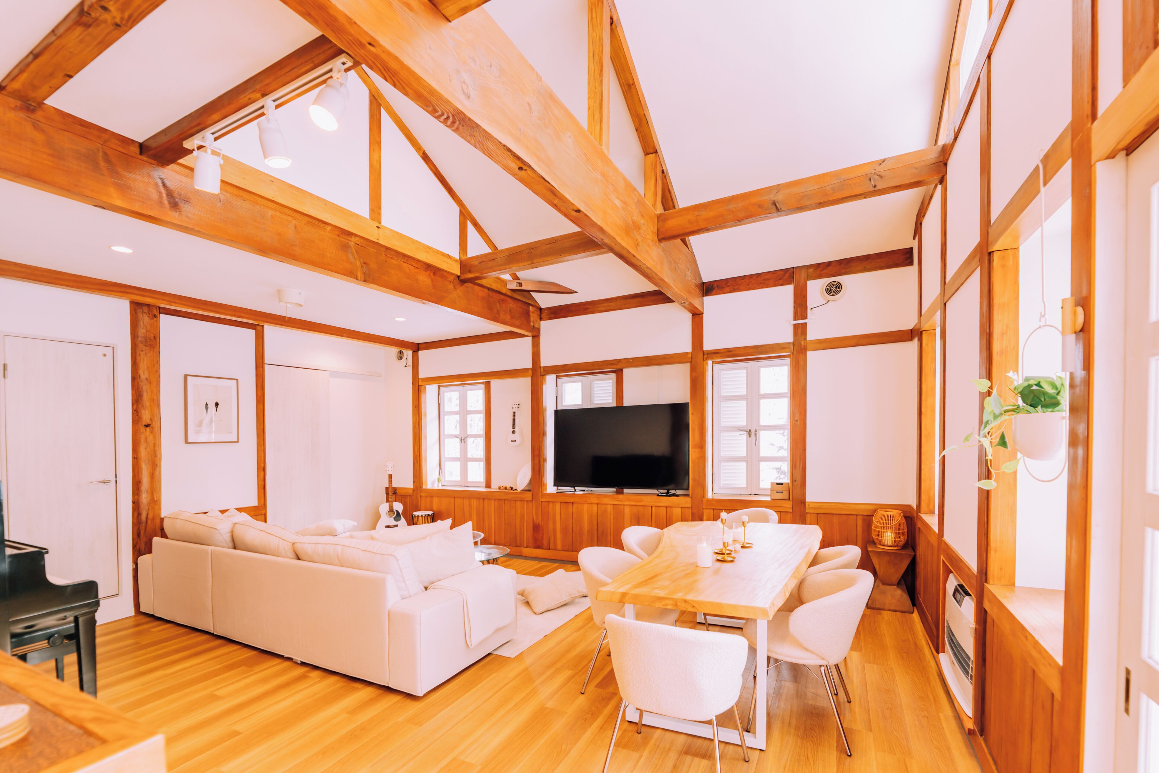 A spacious living area with a wooden ceiling, a large flat-screen TV, a sofa, and a dining table with chairs.