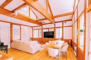 Un salón amplio con techo de madera, un televisor de pantalla plana grande, un sofá y una mesa de comedor con sillas.