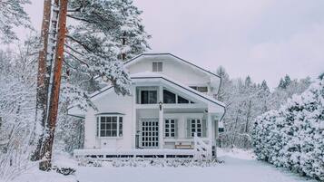 A two-story house with a porch, surrounded by snow-covered trees.