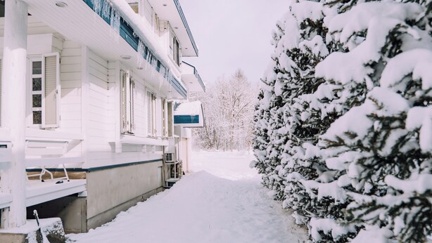 A snow-covered pathway leading to a white building with a blue awning. - Stylish Hakuba Whitegrove Sauna Chalet (Hakuba)