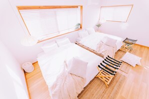 Quarto com duas camas, uma mesinha e uma janela com persianas.