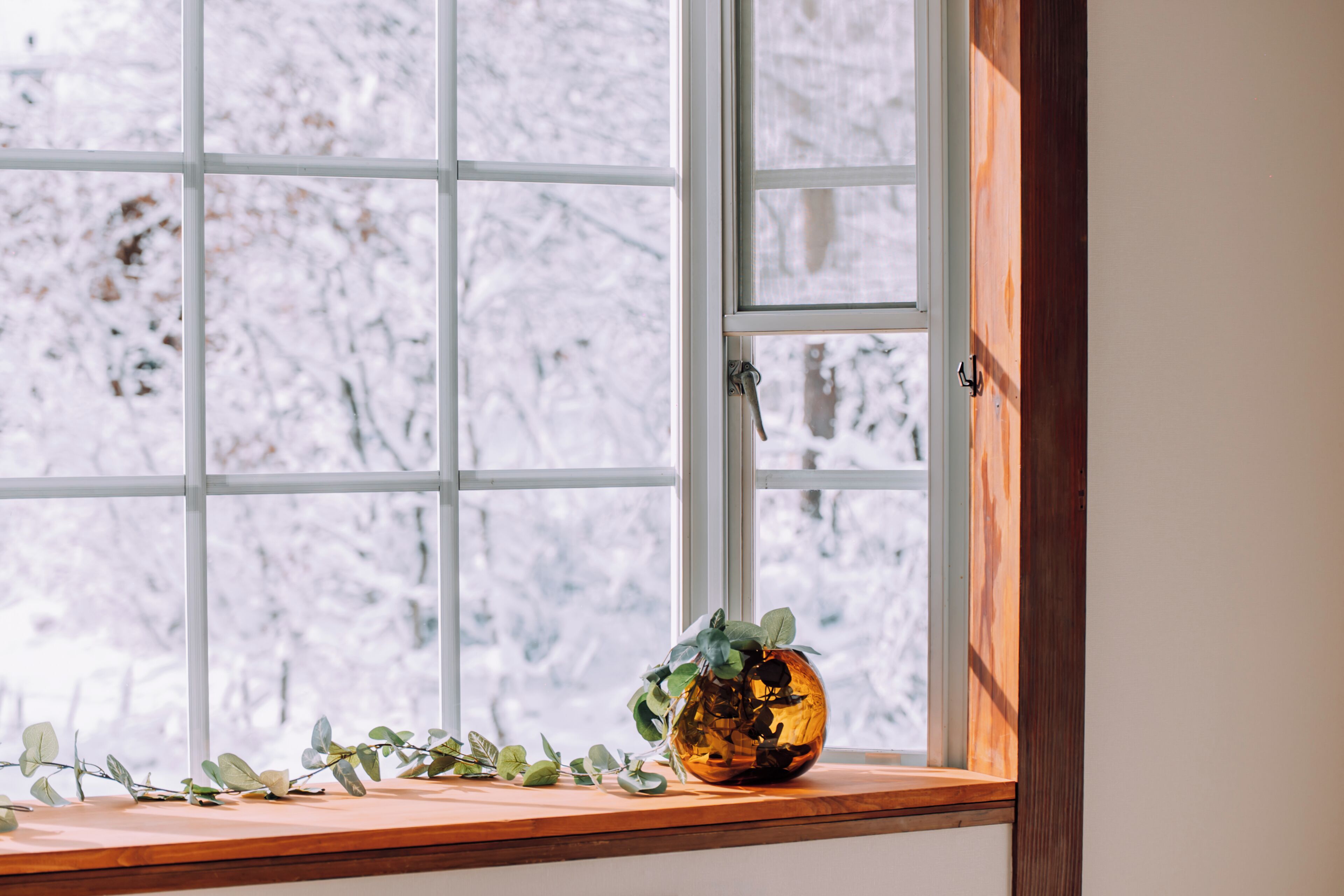 A window with a view of snow-covered trees, a wooden ledge, and a glass vase with greenery.