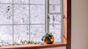 A window with a view of snow-covered trees, a wooden ledge, and a glass vase with greenery. - Stylish Hakuba Whitegrove Sauna Chalet (Hakuba)