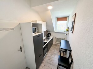 A compact kitchen with a microwave, stove, and sink. There's a small table and a window with a view.