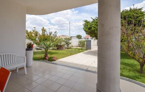 A covered patio area with a white bench, a potted plant, and a view of a residential street with houses and trees. - Amazing home in Ispica with WiFi (Ispica)