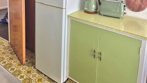A kitchen with green cabinets, a white refrigerator, a green kettle, and a wooden cutting board on the countertop. - Tāhunanui Nest (Nelson)