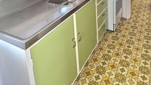 A compact kitchen with a sink, stove, and a small window with a curtain. - Tāhunanui Nest (Nelson)