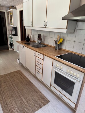 A kitchen with white cabinets, a wooden countertop, a sink, a stove, and a dish rack. - Forest retreat near beach and Rønne (Rønne)