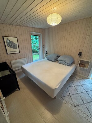 A bedroom with a bed, a radiator, a framed map, and a window. - Forest retreat near beach and Rønne (Rønne)