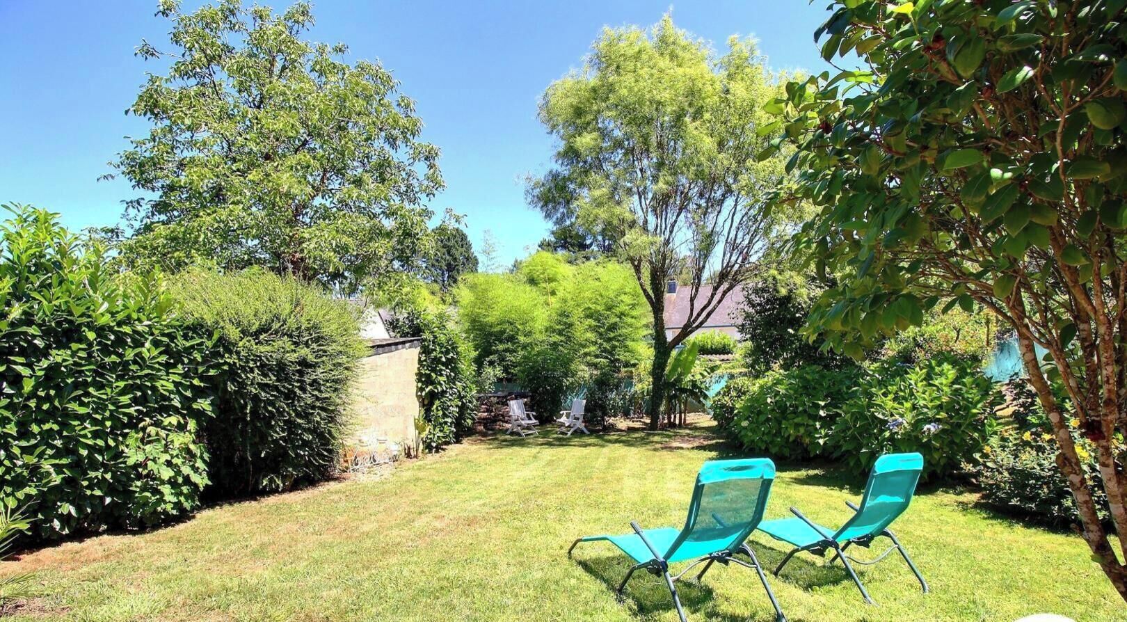 A backyard with a lawn, two green chairs, and various trees and shrubs.