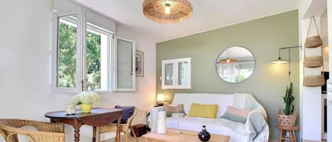 A living room with a sofa, a coffee table, wicker chairs, a round mirror, and a hanging light fixture.