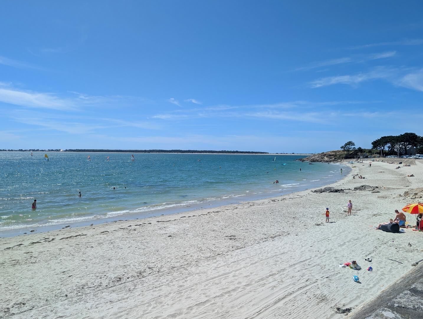 A beach with clear blue water, sandy shore, and a few people.
