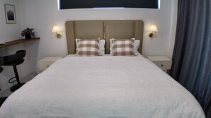 A neatly made bed with a headboard, two bedside lamps, a small table with a plant, and a chair. - Taupō Premium Retreat | Private Spa, Ensuite & BBQ (Taupō)