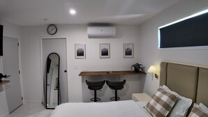 A bedroom with a bed, a desk with two chairs, a clock, and three framed pictures on the wall.