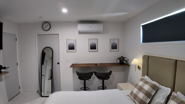 Een slaapkamer met een bed, een bureau met twee stoelen, een klok en drie ingelijste foto's aan de muur.