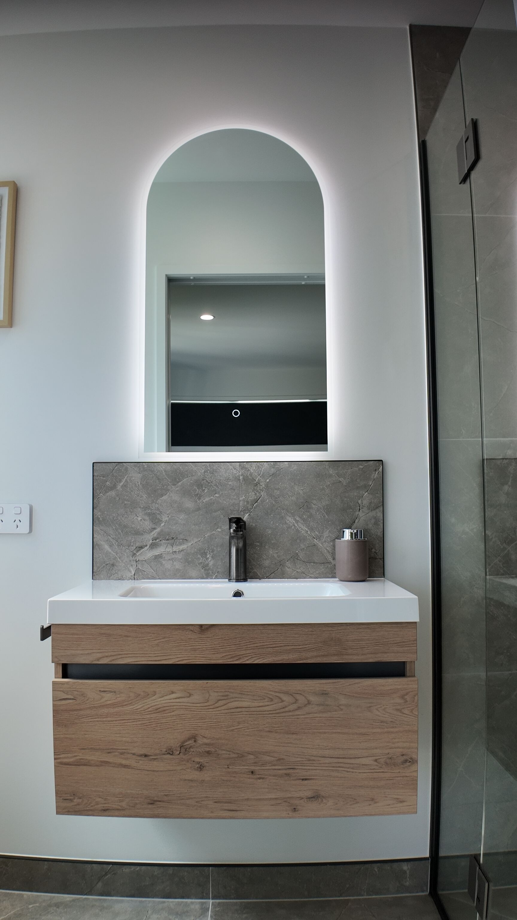 A modern bathroom with a white vanity, a mirror with an arch above it, and a shower area.