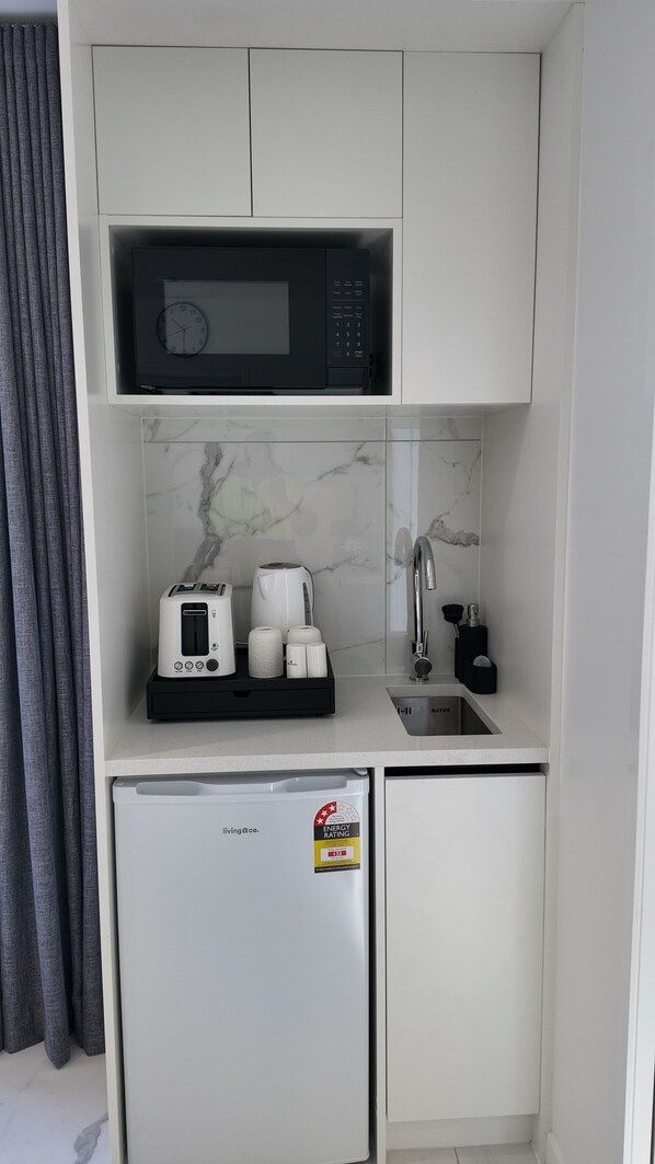 A compact kitchenette with a microwave, toaster, coffee maker, and a small refrigerator.