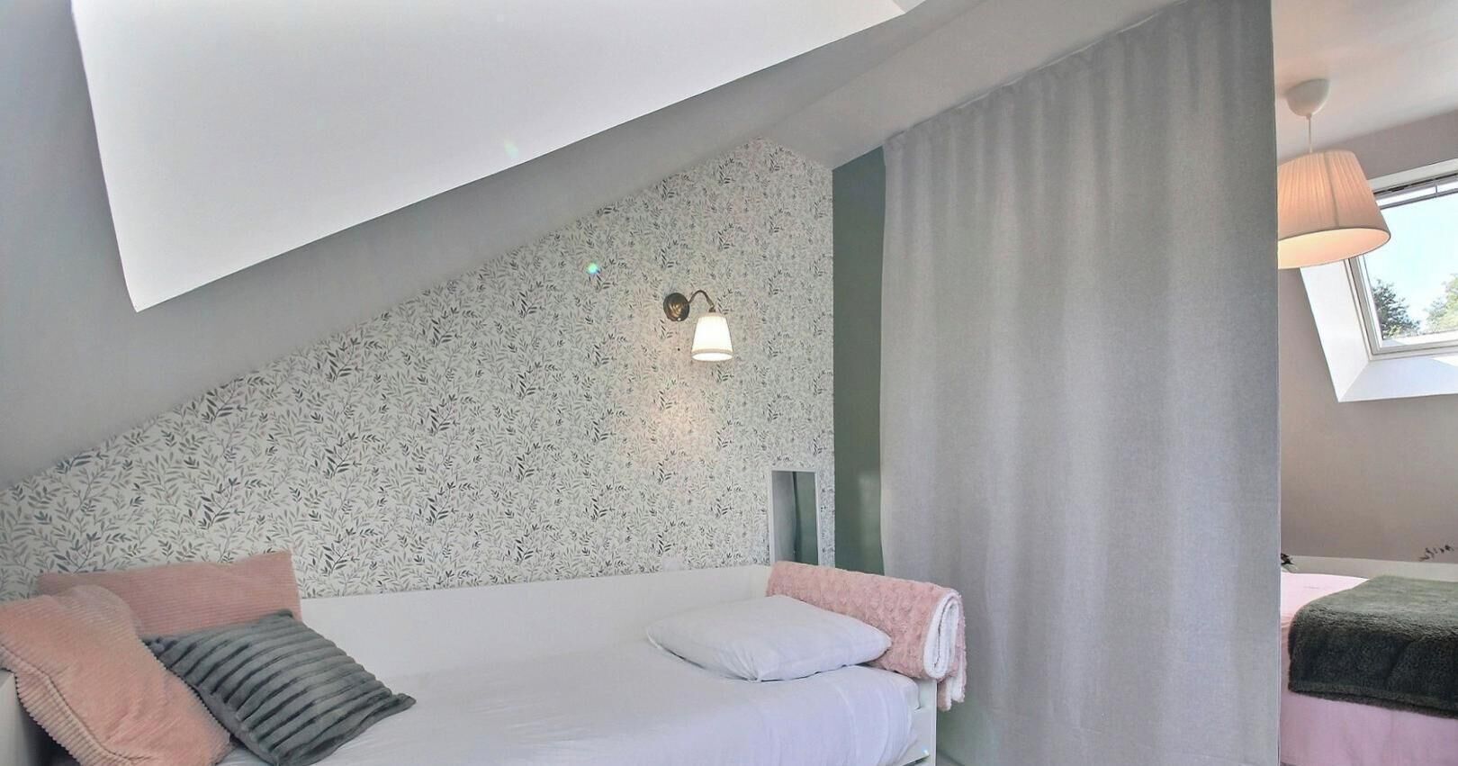 A bedroom with a bed, a headboard, a wall-mounted light, and a window with curtains.