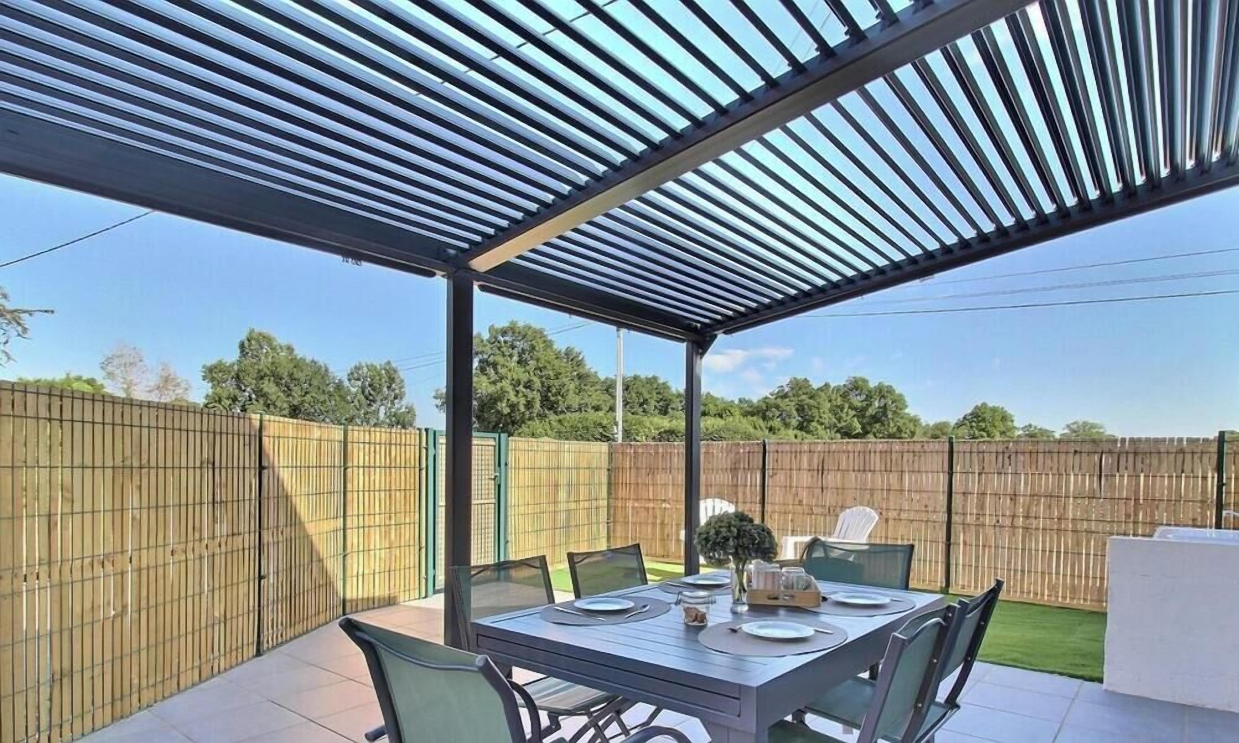 An outdoor patio with a table set for dining, surrounded by chairs, under a metal roof structure.