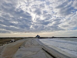 Eine Küstenstraße führt zu einer weißen Kirche mit einem Kirchturm, einem Sandstrand und einem bewölkten Himmel.