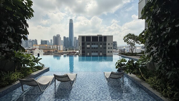 Piscina infinita en la azotea con sillones de descanso, rodeada de follaje y vistas a un horizonte urbano con edificios modernos.