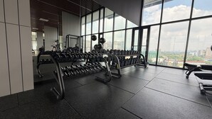 Un gimnasio con equipo de ejercicio y amplias ventanas con vistas a la ciudad.